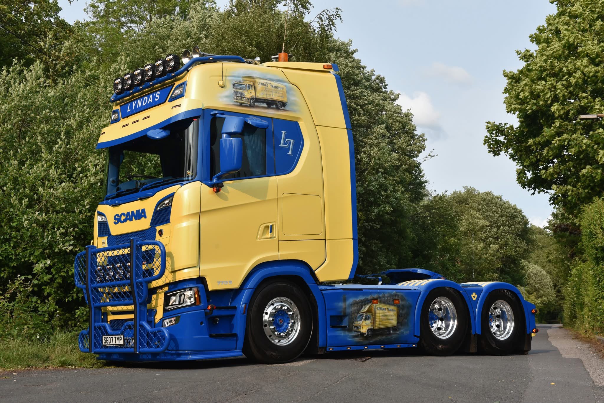 Yellow and blue Lynda's Transport Scania tractor unit on a country lane